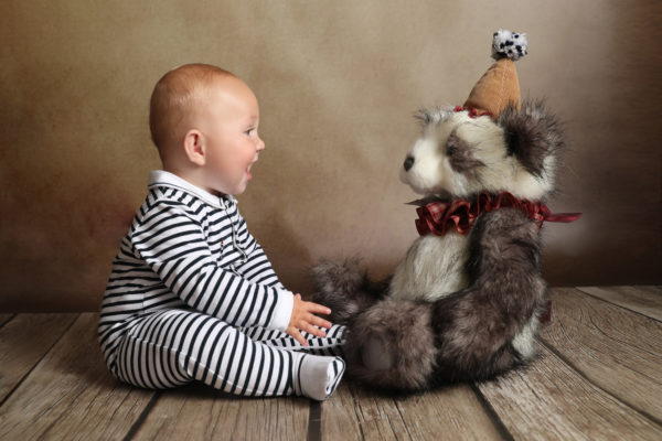 baby photoshoot little boy toddler in striped onesie smiling at teddy bear