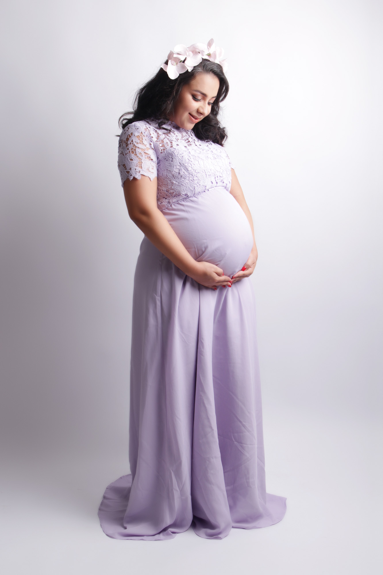 professional portrait of pregnant woman in lilac dress and flower crown holding bump
