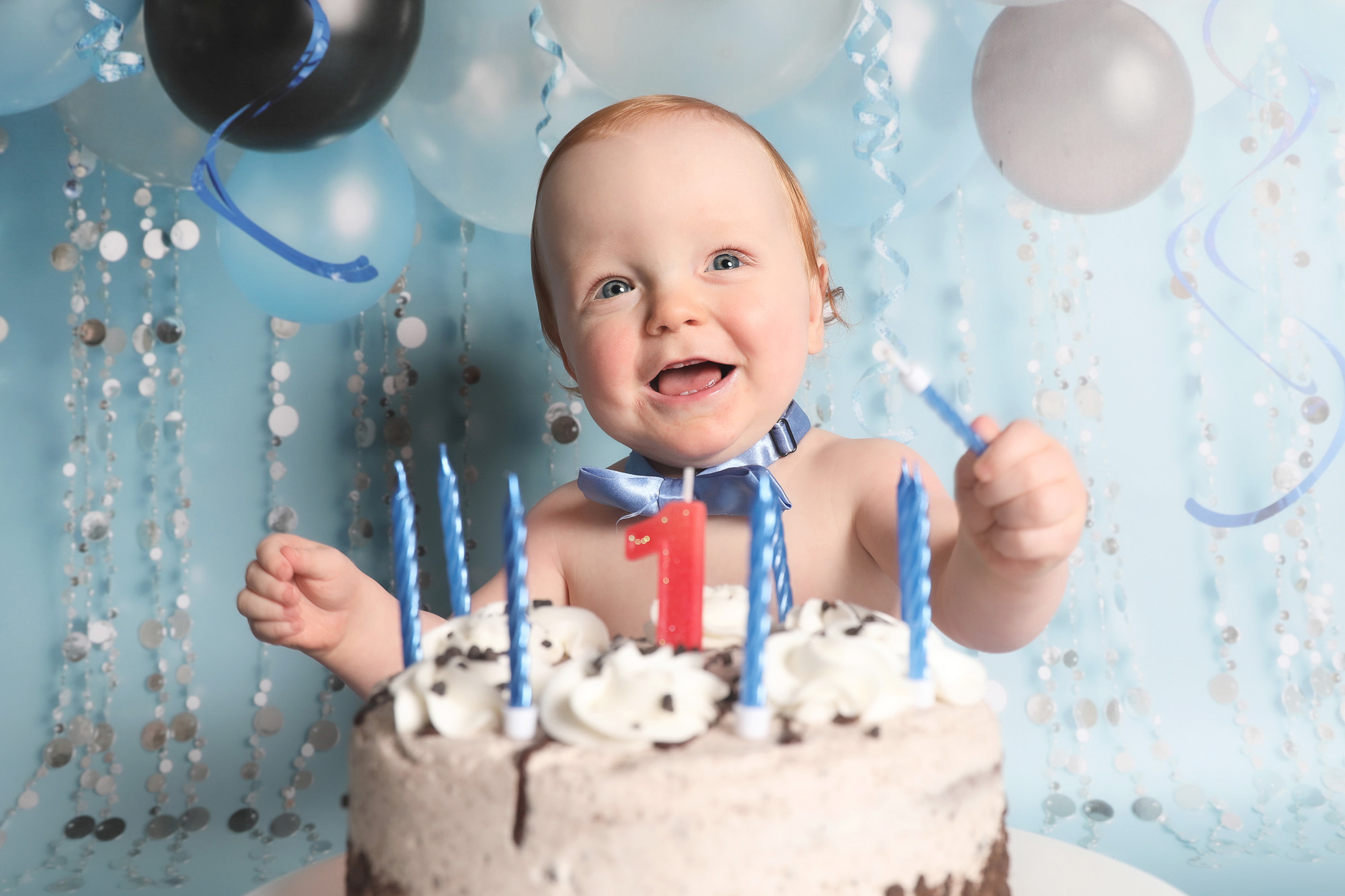 first birthday cakesmash baby boy toddler cakesmash photoshoot with blue balloon streamers backdrop