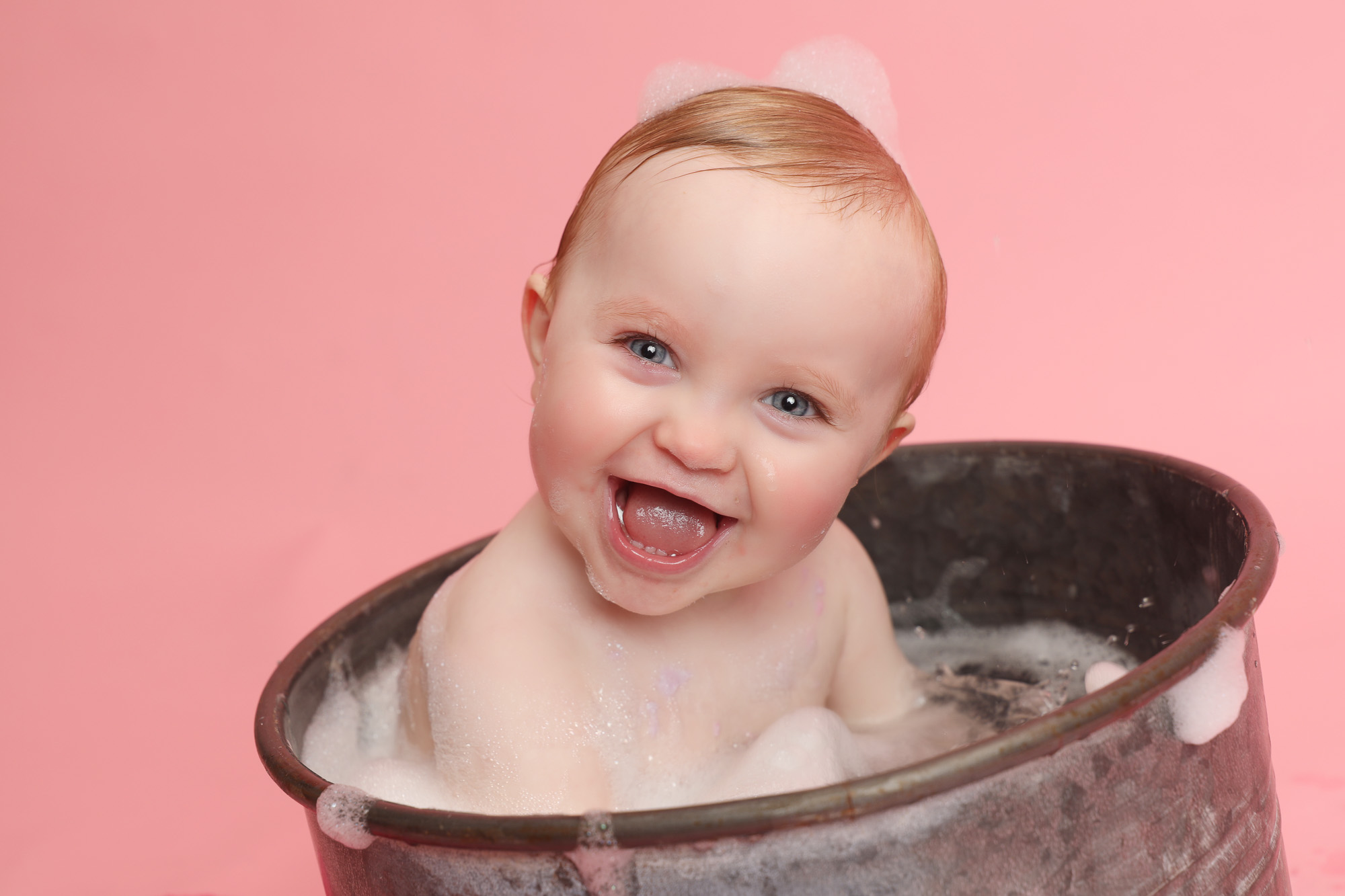 baby girl in tin bubble bath tub smiling on pink backdrop