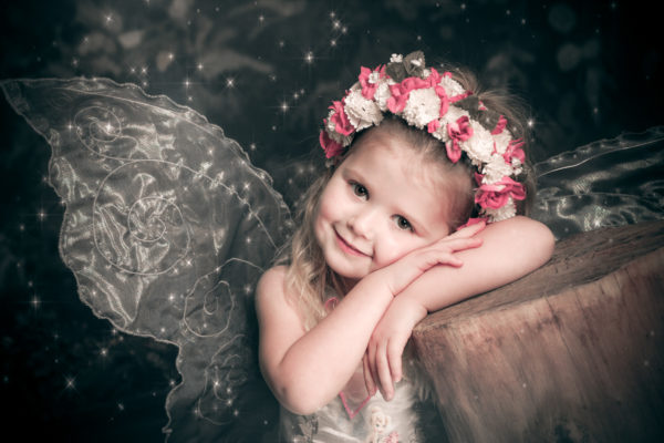 little girl dressed as fairy with wings and flower headband in enchanted woodland photoshoot
