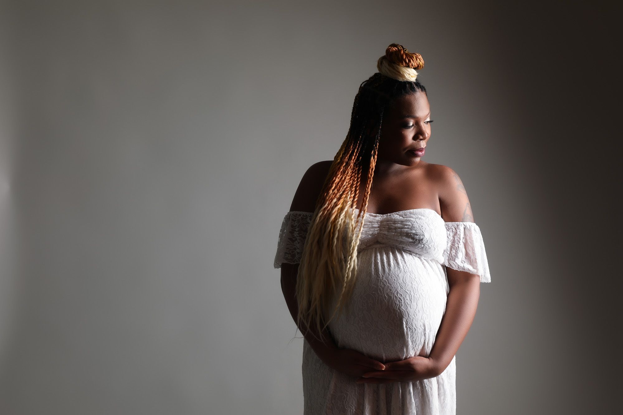 pregnant woman with braids in white lace dress cradling bump