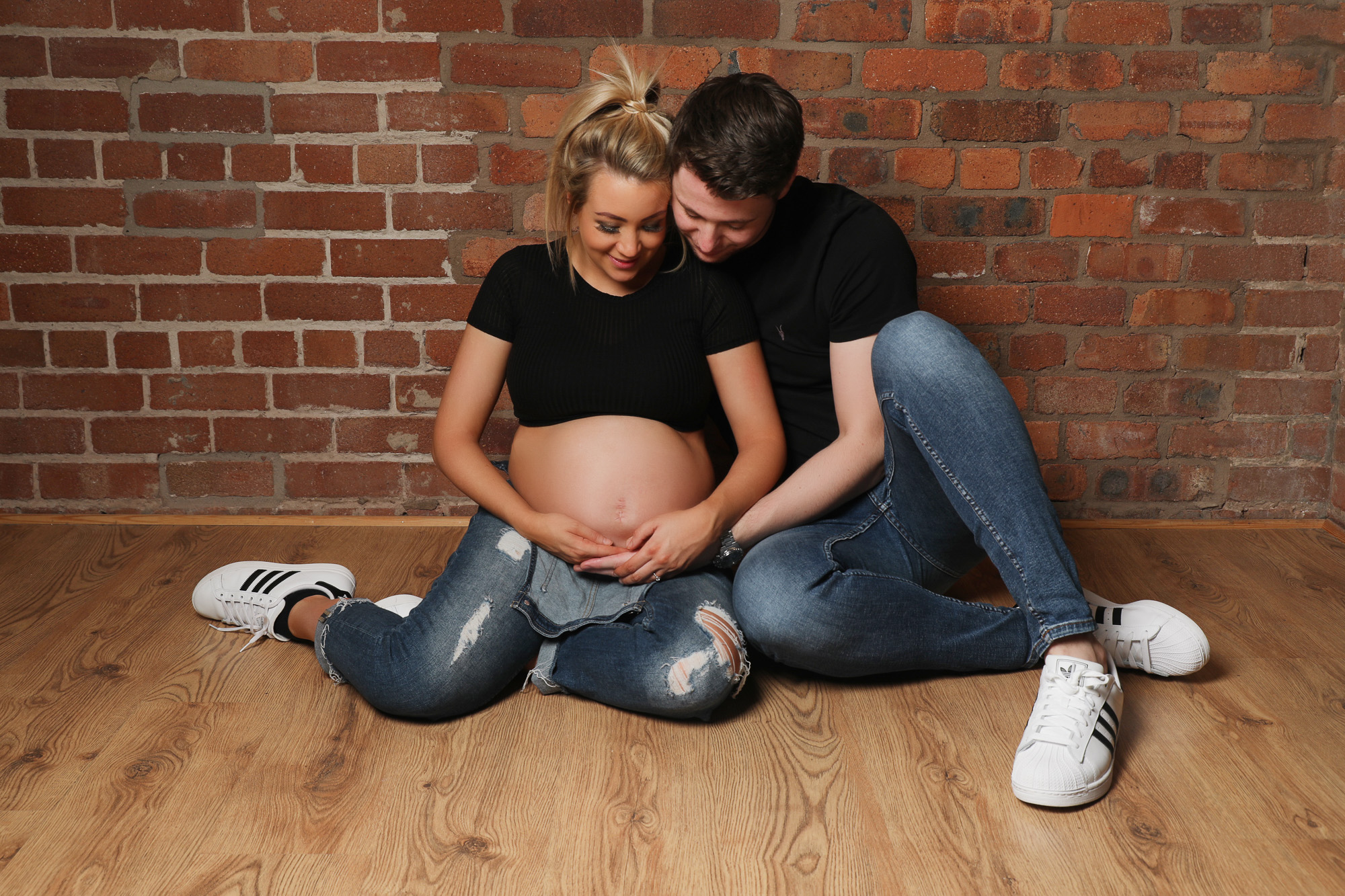 maternity photo shoot couple in matching black t shirts and denim jeans both cradling the woman's bump