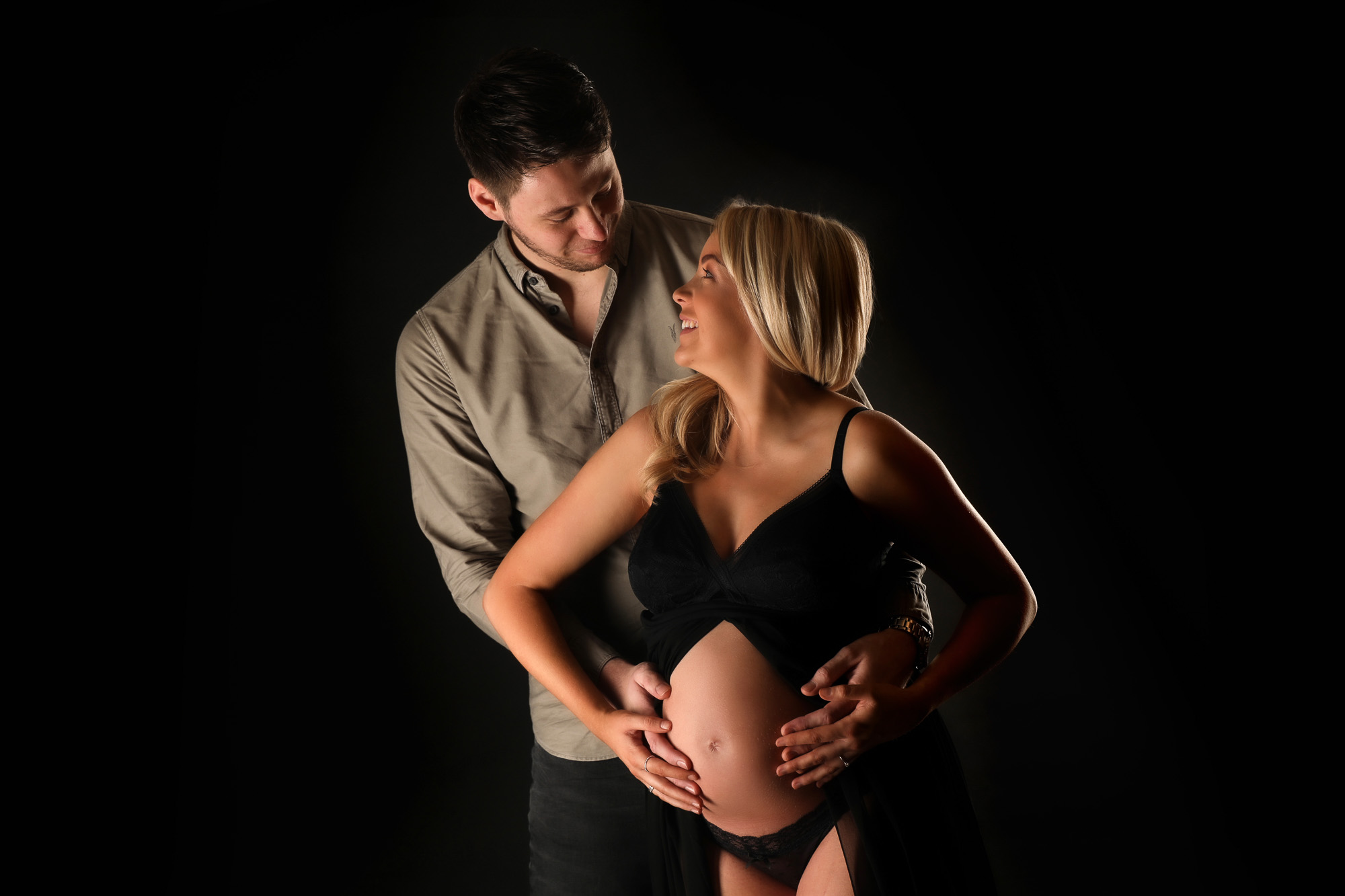 pregnant woman with partner looking at each other holding bump