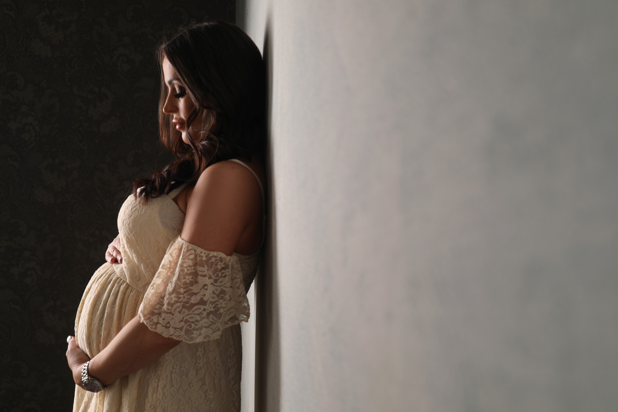 pregnant woman in lace dress leaning on wall holding bump