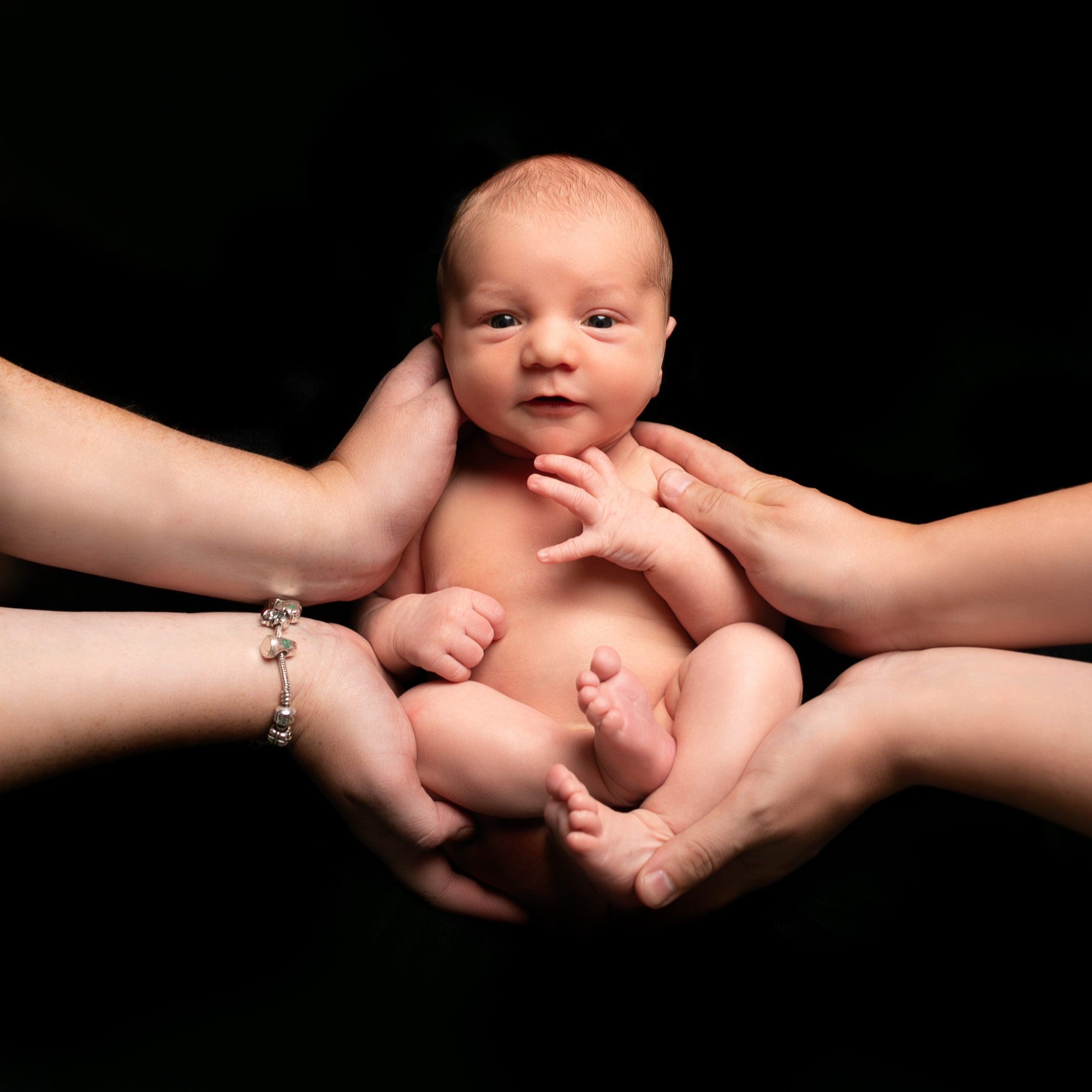 newborn photoshoot baby awake being cradled by parents hands on black background