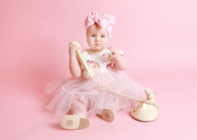 Little sitters baby toddler Photoshoot Peekaboo Liverpool baby girl in tutu and hair bow playing with vintage telephone pink