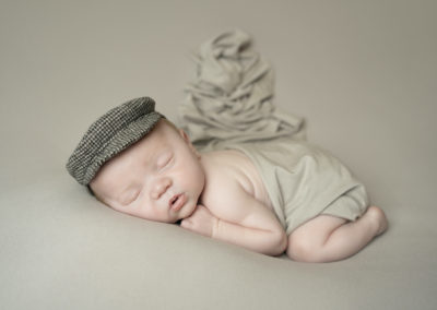 Newborn photoshoot Peekaboo Liverpool baby in flatcap on neutral backdrop