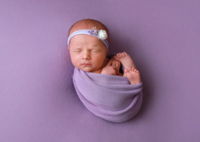 Newborn photoshoot Peekaboo Liverpool baby girl swaddled in lilac wrap