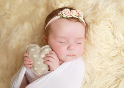 Newborn photoshoot Peekaboo Liverpool baby holding neutral heart on creamy backdrop