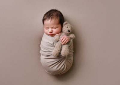 Newborn photoshoot Peekaboo Liverpool baby on neutral backdrop holding teddy