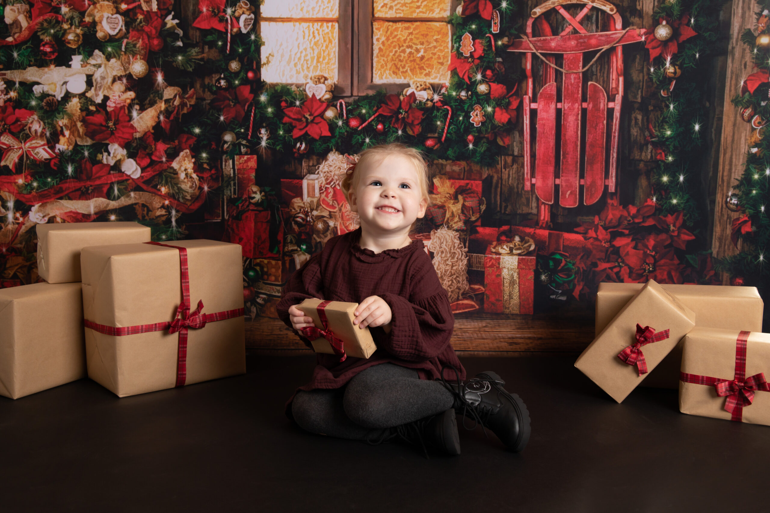 little girl sitting by gold decorated christmas tree with gifts